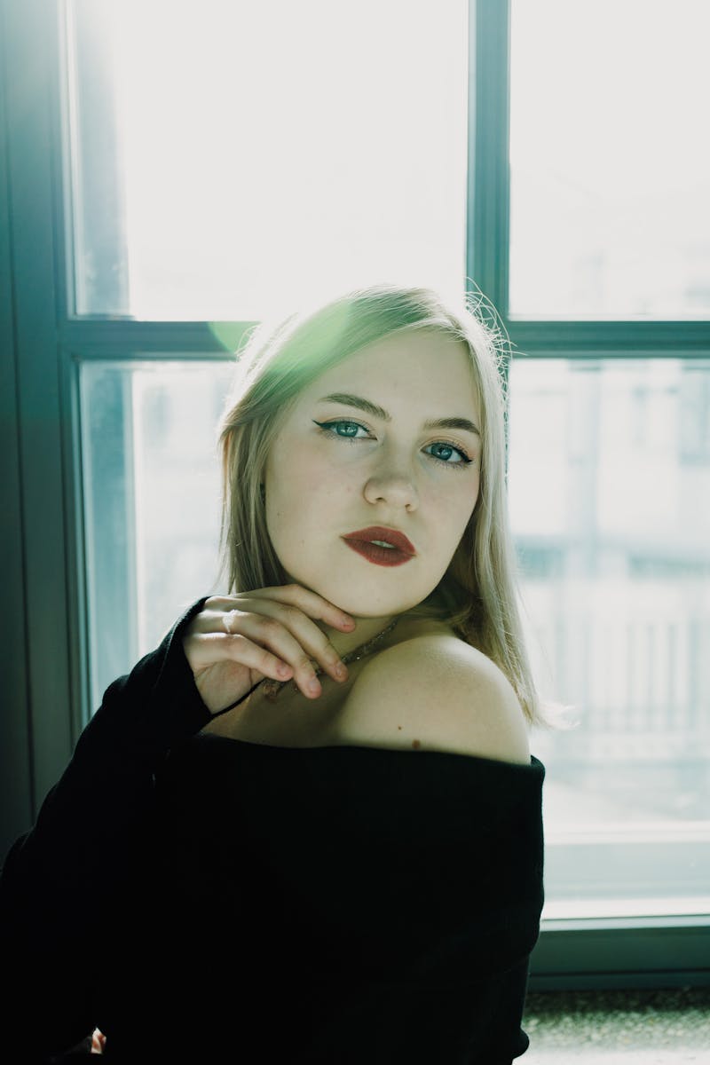 Graceful portrait of a young woman with dramatic lighting near a window, exuding elegance.